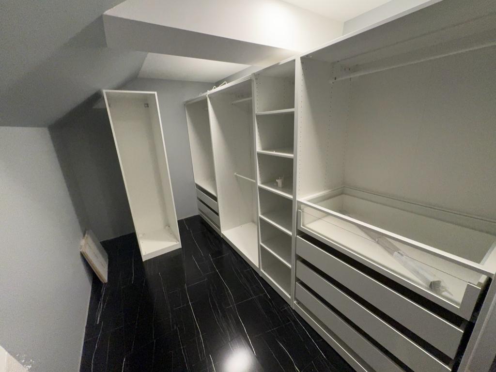 A sleek white wardrobe system fitted under a sloped ceiling with dark flooring, highlighting an expert custom closet installation Maryland that utilizes awkward spaces.