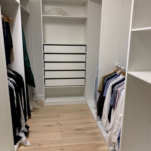 A fully organized luxury white walk-in closet with hanging clothes and black-trimmed drawers, the result of a premium custom closet installation Maryland.